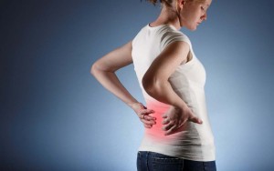 A lady grips the small of her back with both hands. The lower back is highlighted in a red tinge to show pain and discomfort. This is to illustrate structural problems.